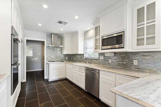 kitchen featuring white cabinets, light stone counters, wall chimney exhaust hood, and appliances with stainless steel finishes