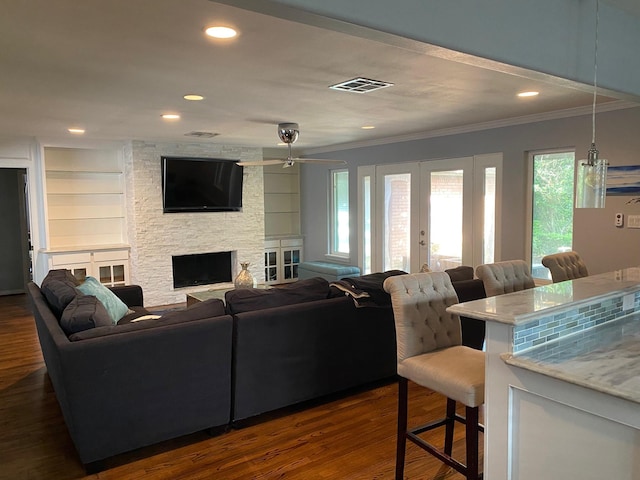 living room featuring french doors, a fireplace, visible vents, dark wood-type flooring, and ornamental molding