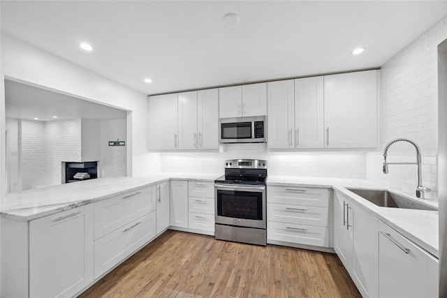 kitchen with stainless steel appliances, kitchen peninsula, decorative backsplash, sink, and white cabinetry