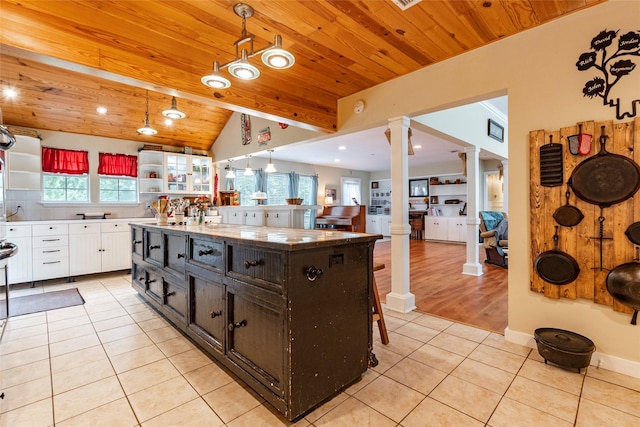 kitchen featuring ornate columns, light tile patterned floors, decorative light fixtures, a center island with sink, and white cabinets