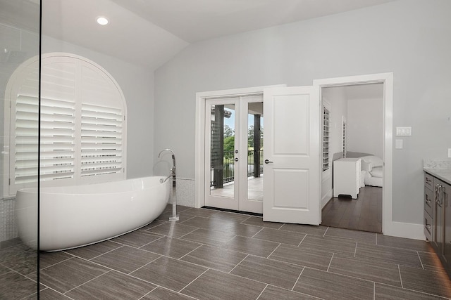 bathroom with a tub, french doors, vanity, and vaulted ceiling