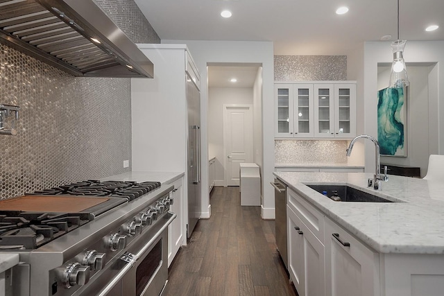 kitchen with light stone counters, wall chimney exhaust hood, sink, high quality appliances, and white cabinets