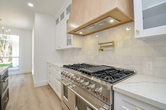 kitchen featuring premium range hood, light stone countertops, white cabinets, and range with two ovens