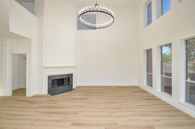 unfurnished living room featuring a chandelier, light hardwood / wood-style floors, a towering ceiling, and a tiled fireplace