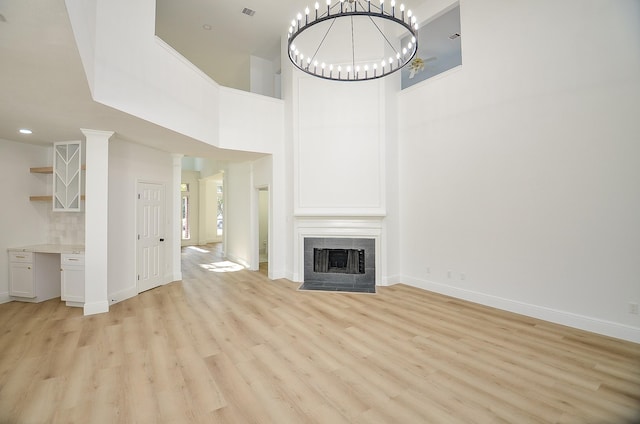 unfurnished living room with light hardwood / wood-style flooring, a chandelier, and a high ceiling