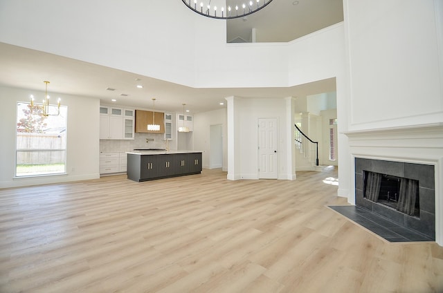 unfurnished living room featuring a chandelier, light hardwood / wood-style floors, a towering ceiling, and a tiled fireplace