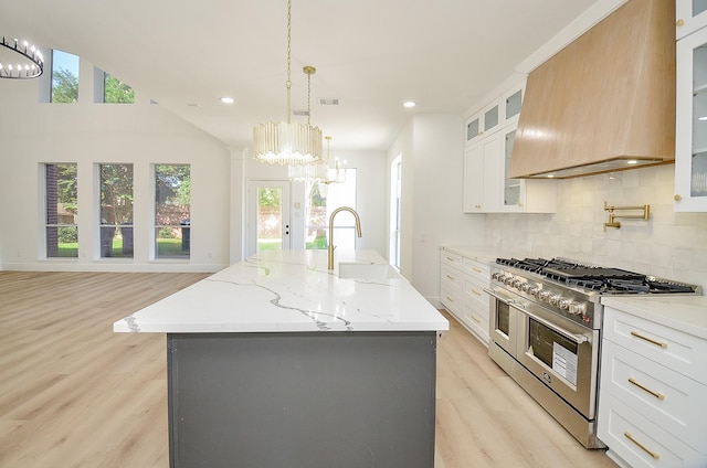 kitchen featuring pendant lighting, a kitchen island with sink, range with two ovens, custom range hood, and white cabinetry