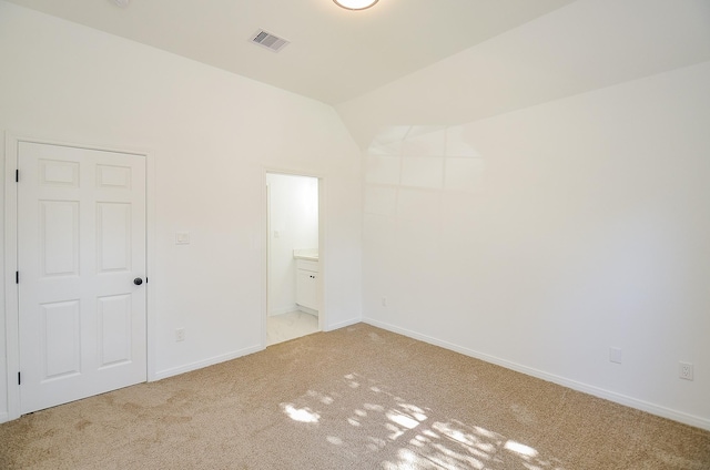 unfurnished bedroom with ensuite bathroom, light colored carpet, and vaulted ceiling