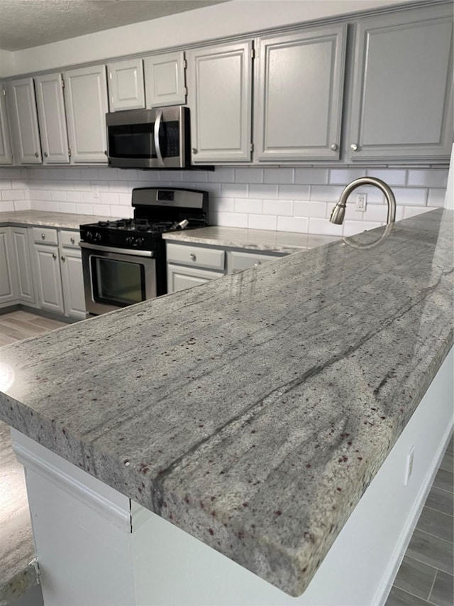 kitchen with backsplash, light stone counters, gray cabinetry, and stainless steel appliances