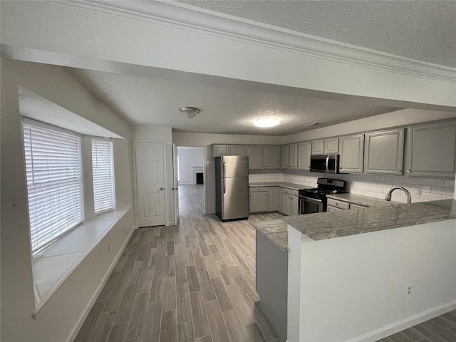 kitchen with gray cabinetry, backsplash, a textured ceiling, kitchen peninsula, and stainless steel appliances