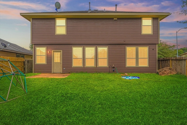 back house at dusk featuring a patio area and a yard