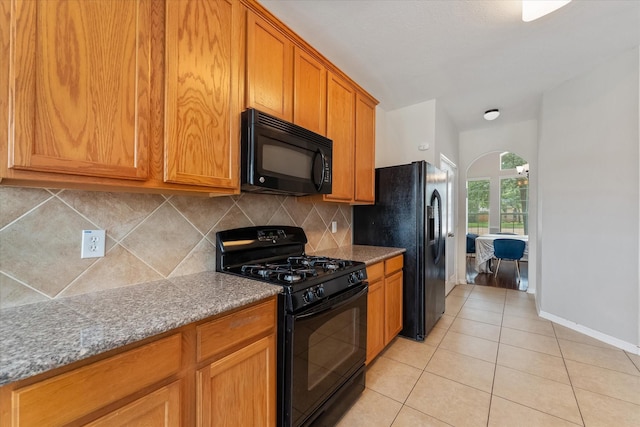 kitchen with black appliances, light tile patterned flooring, light stone countertops, and tasteful backsplash