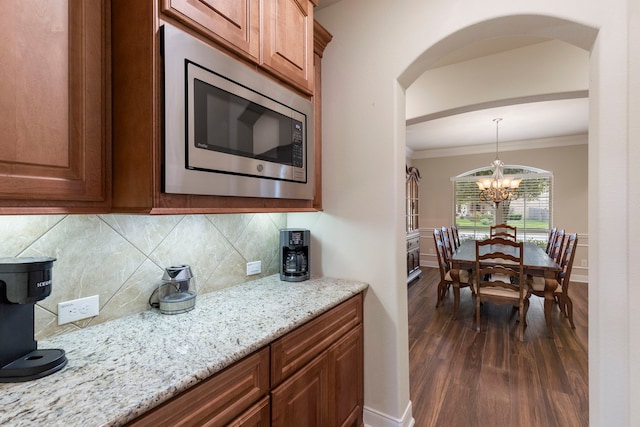 kitchen with stainless steel microwave, light stone counters, backsplash, crown molding, and a chandelier