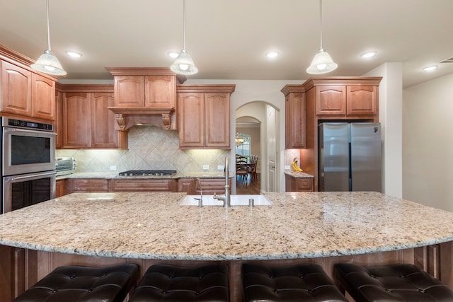 kitchen with a large island with sink, stainless steel appliances, decorative light fixtures, and a kitchen breakfast bar