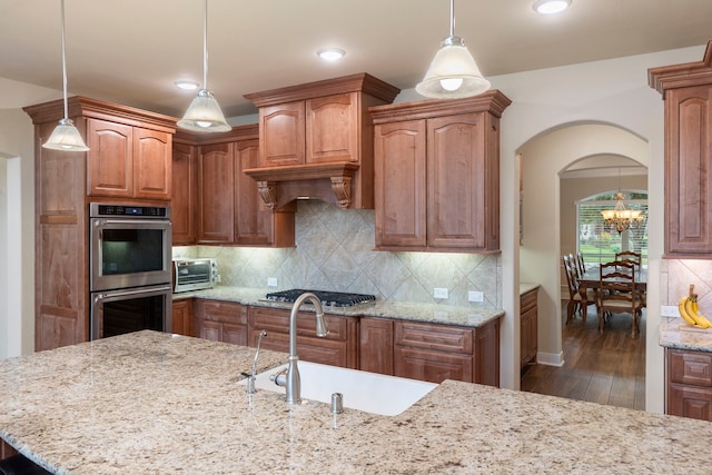 kitchen featuring light stone countertops, tasteful backsplash, stainless steel appliances, sink, and decorative light fixtures