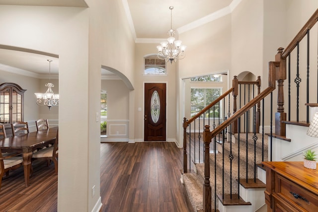 foyer entrance with dark hardwood / wood-style floors, ornamental molding, a towering ceiling, and an inviting chandelier