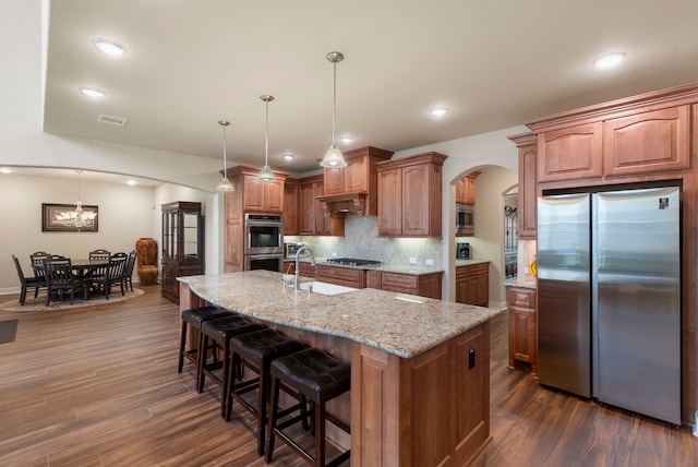 kitchen with dark wood-type flooring, decorative light fixtures, stainless steel appliances, and a center island with sink