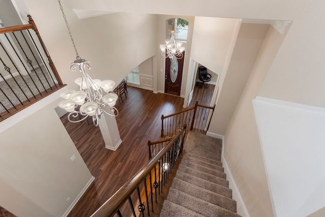 stairs with wood-type flooring and an inviting chandelier