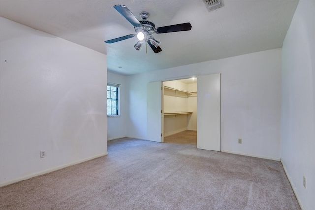 interior space with ceiling fan, a walk in closet, light carpet, and a closet