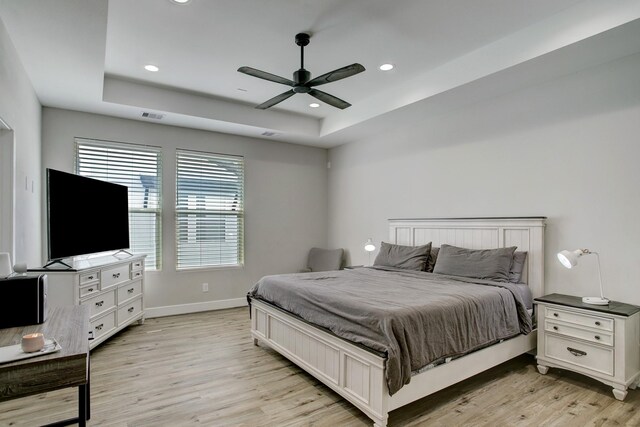 bedroom featuring light hardwood / wood-style flooring, a raised ceiling, and ceiling fan