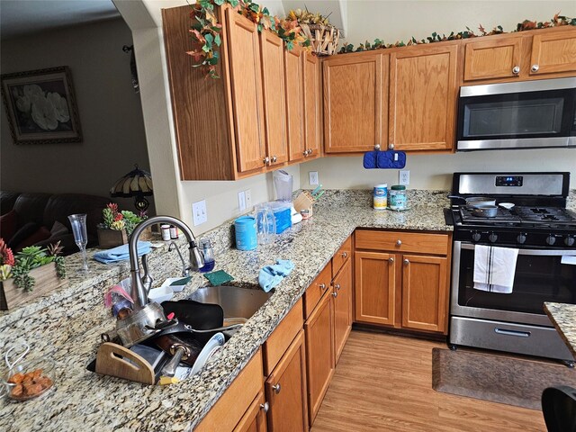 kitchen with light stone countertops, sink, stainless steel appliances, and light hardwood / wood-style floors