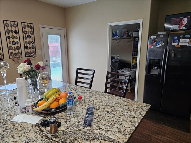 kitchen with dark hardwood / wood-style floors, light stone countertops, and black refrigerator with ice dispenser