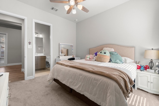 bedroom with ceiling fan, ensuite bathroom, and light carpet