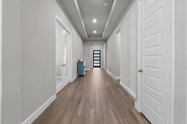 hallway with a raised ceiling, light wood-type flooring, and french doors