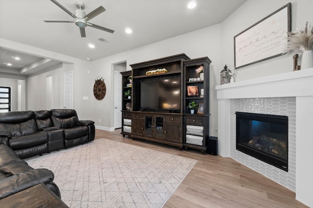 living room featuring a tile fireplace, light hardwood / wood-style floors, and ceiling fan