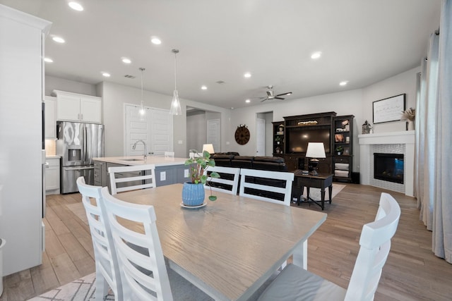 dining room featuring sink, light hardwood / wood-style flooring, ceiling fan, and a tiled fireplace