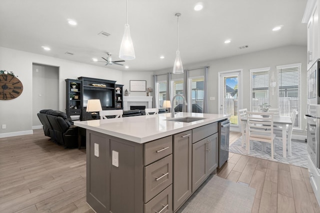 kitchen featuring ceiling fan, sink, hanging light fixtures, stainless steel dishwasher, and a kitchen island with sink