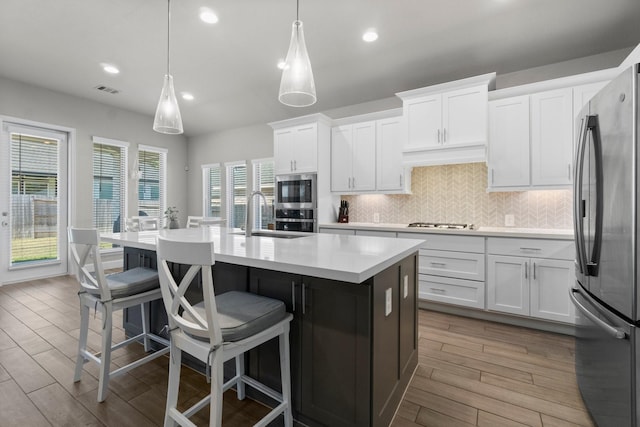 kitchen featuring tasteful backsplash, stainless steel appliances, decorative light fixtures, white cabinets, and an island with sink