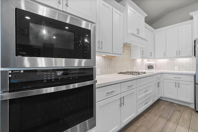 kitchen featuring premium range hood, white cabinets, stainless steel appliances, and lofted ceiling