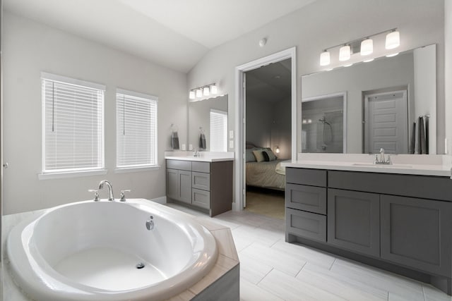 bathroom with tile patterned floors, vanity, tiled bath, and vaulted ceiling