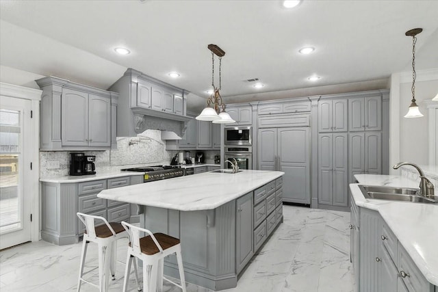 kitchen featuring gray cabinetry, built in appliances, a kitchen island with sink, and hanging light fixtures