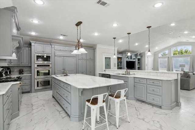 kitchen with backsplash, a large island with sink, gray cabinets, hanging light fixtures, and lofted ceiling