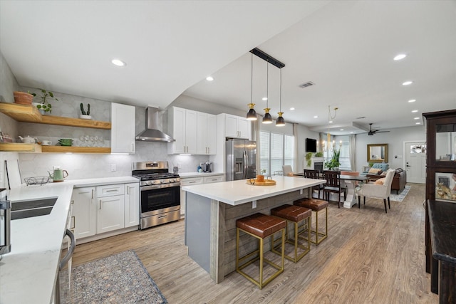 kitchen featuring white cabinets, wall chimney range hood, ceiling fan, decorative backsplash, and stainless steel appliances