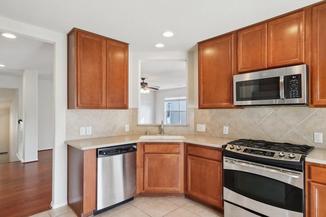 kitchen with light countertops, appliances with stainless steel finishes, a sink, and brown cabinets