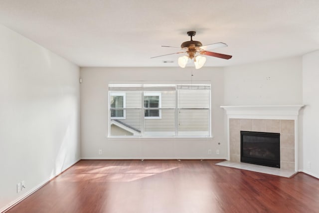 unfurnished living room with baseboards, ceiling fan, a tiled fireplace, and wood finished floors