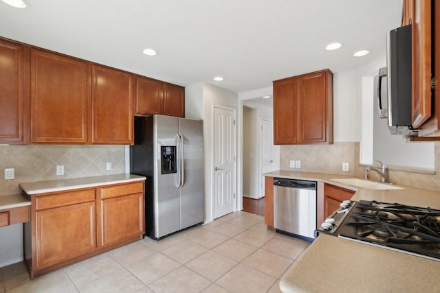 kitchen with stainless steel appliances, light countertops, brown cabinetry, light tile patterned flooring, and a sink