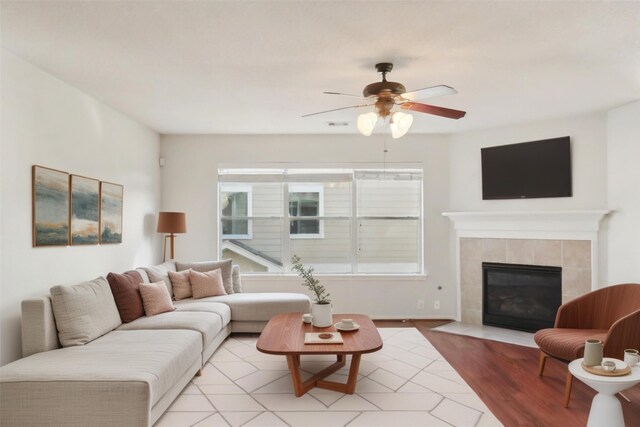 living room featuring ceiling fan, light hardwood / wood-style floors, and a tile fireplace