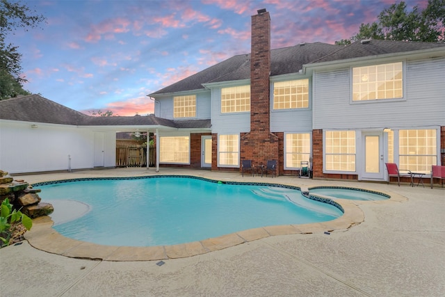 pool at dusk featuring an in ground hot tub and a patio