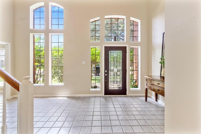 foyer with light tile patterned floors, stairway, a towering ceiling, and baseboards