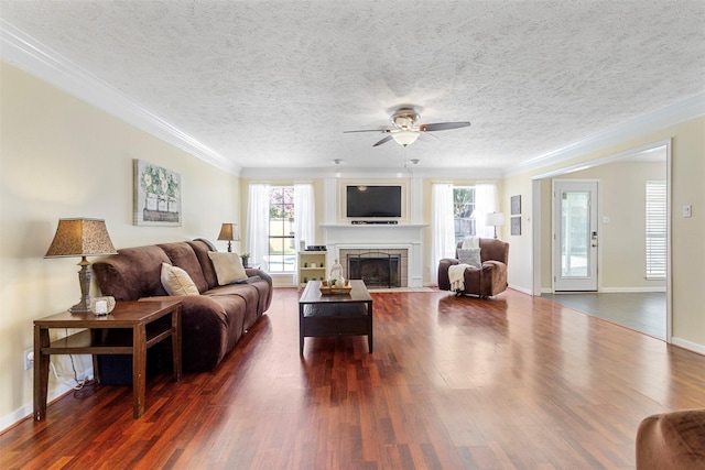 living room with ceiling fan, dark hardwood / wood-style flooring, a stone fireplace, and crown molding