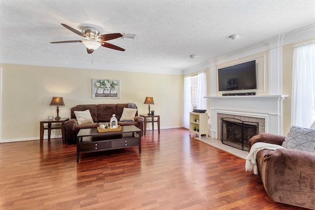 living room featuring crown molding, wood-type flooring, a textured ceiling, and a tiled fireplace