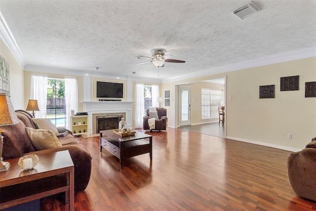 living room with dark wood-type flooring, a stone fireplace, ceiling fan, and ornamental molding