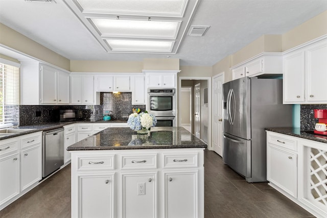 kitchen featuring stainless steel appliances, white cabinetry, a kitchen island, and dark stone countertops