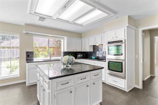 kitchen featuring stainless steel double oven, sink, dark stone countertops, white cabinets, and a kitchen island