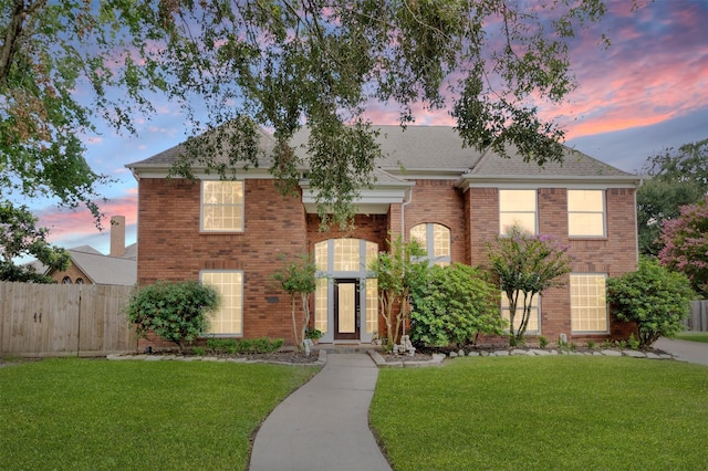 view of front facade featuring a shingled roof, brick siding, fence, and a front lawn