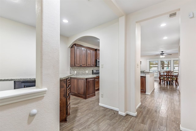 kitchen featuring ceiling fan, light stone counters, tasteful backsplash, and light hardwood / wood-style flooring